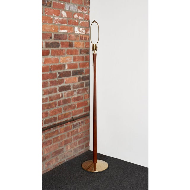 Simple, elegant floor lamp sculpted from solid teak with slender, cylindrical, tapered stem supported by dense round brass...