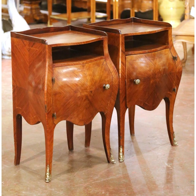 Crafted in France circa 1920, this elegant pair of antique Louis XV-style bedside tables features graceful bombé...