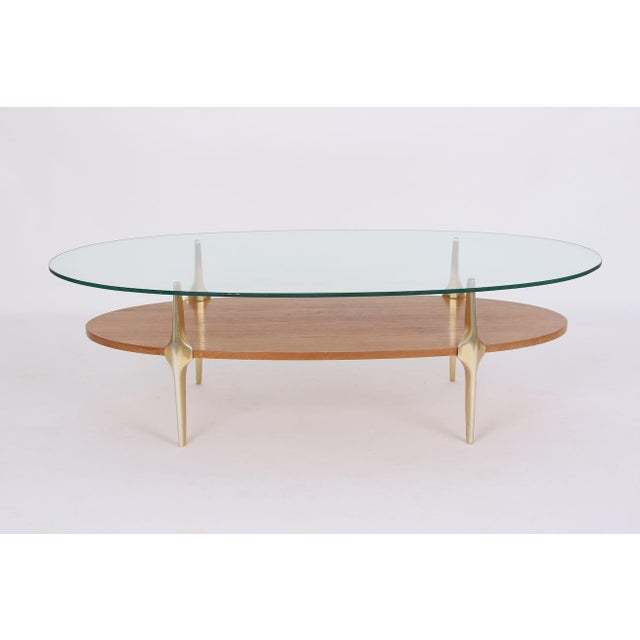 Elegant coffee table with brass legs, oak shelf, and glass top. Beautiful Italian design with a light, natural patina. The...