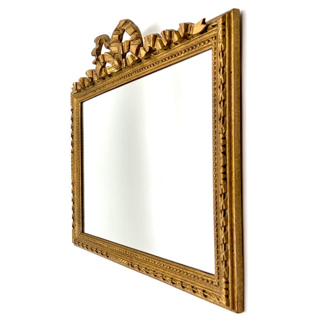 A beautiful mid century French carved giltwood rectangular mirror with beaded trim and a hand carved bow and ribbon in a...