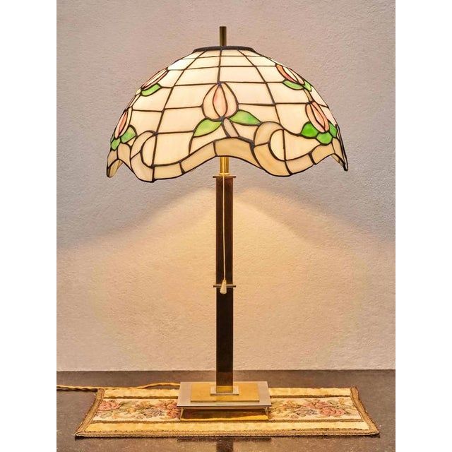 Designer lamp with glass shade in Tiffany style. Lamp body made of polished brass in gold and white. The shade is made of...