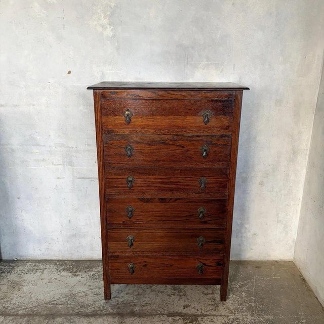 A handsome early 20th-century Arts & Crafts oak tallboy with six full-width drawers, decorative metal drop handles and a...