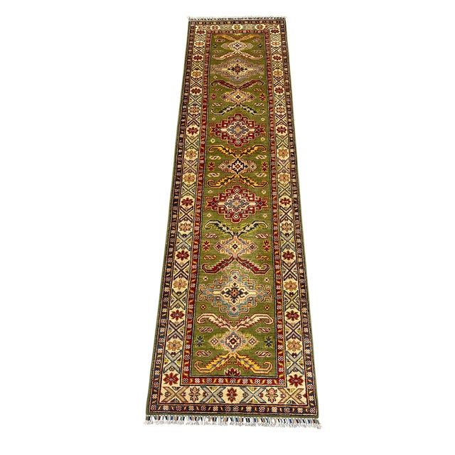 An olive green field anchors this natural-dyed wool runner. Alternating geometric medallions and branching tribal motifs...
