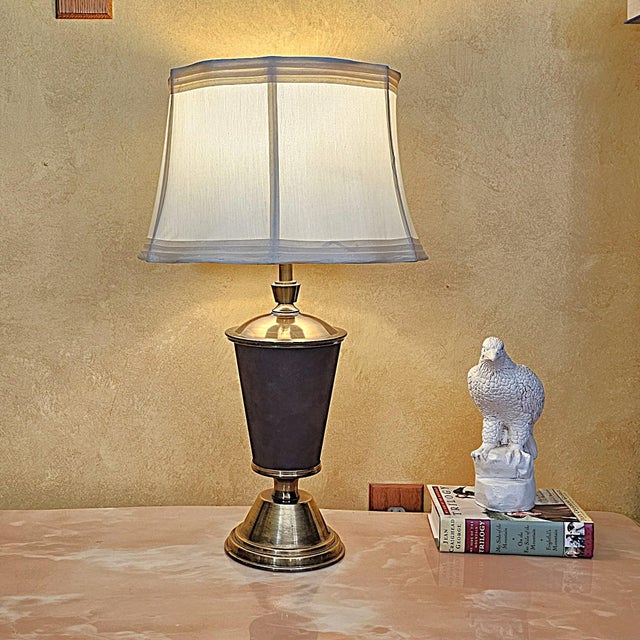 This vintage table lamp features a brass base wrapped in rich faux leather, giving it a warm, classic look accented by an...