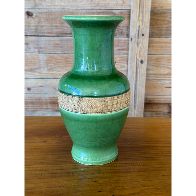 A striking vintage ceramic vase featuring a richly shaded green glaze and a contrasting band of natural fiber wrapping....