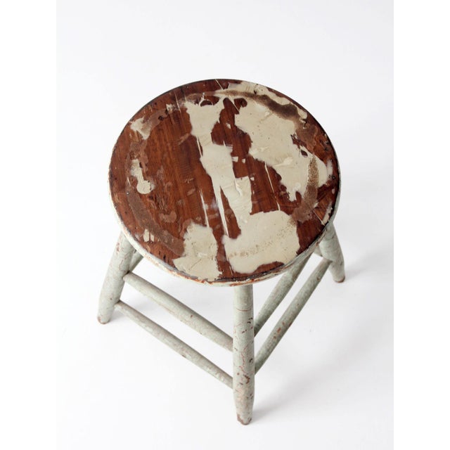 A vintage painted wood stool with a round seat and tapered legs joined by simple stretchers. The soft green finish...