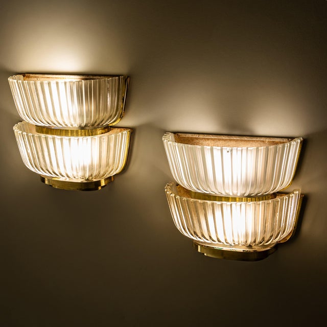 Pair of two-tier wall lights with shades in wavy clear glass and elegant brass mounts. Attributed to Archimede Seguso, the...