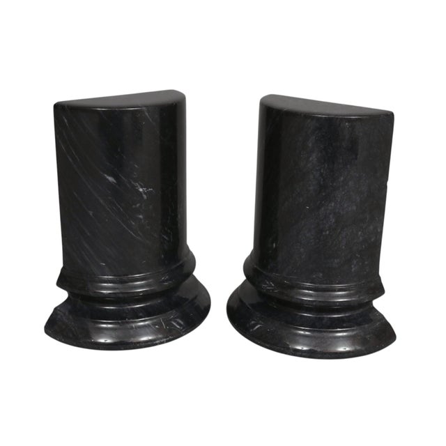A pair of black marble column bookends with white veining. Demilune shaped bookends are carved to give the look of...