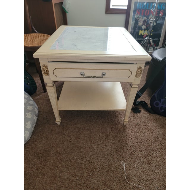 This vintage French Provincial style cream-painted end table features an inlaid marble top insert and a single drawer.