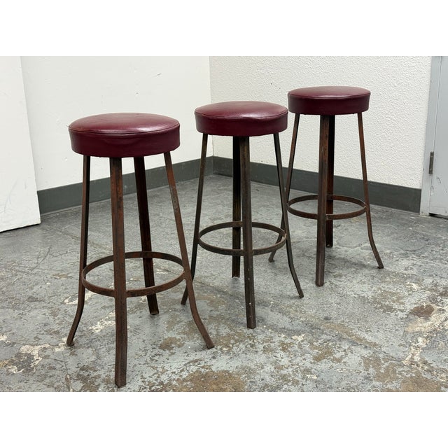 Design Plus Gallery present a Set of Three Mid 20th Century Barstools. The stools have round burgundy vinyl upholstered...