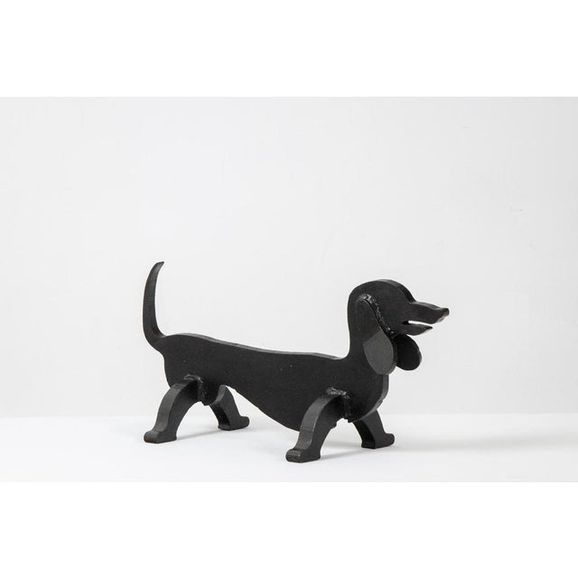 Edouard Shenck. Pair of zoomorphic wrought-iron andirons with a black patina, shaped like dachshunds. Made in France in...