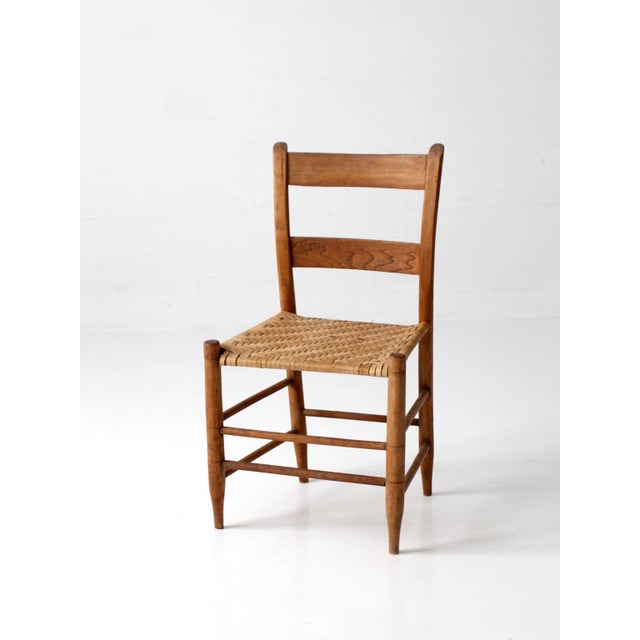 This antique ladderback chair features a warm honey brown finish, a handwoven herringbone splint seat, and a softly shaped...
