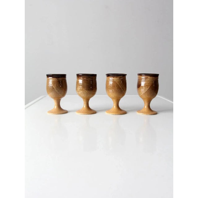 Set of four vintage studio pottery chalices showcasing the beauty of handcrafted ceramic design. Each wine glass features...