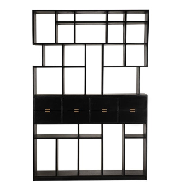 A modern, Hand-Rubbed Black bookcase with eight drawers, brass pulls, and asymmetrical open shelving. Its geometric design...