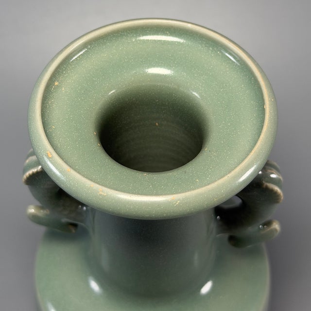 This handmade Longquan celadon vase is fitted with a pair of carved dragon‑form side handles. Smooth glaze covers the...