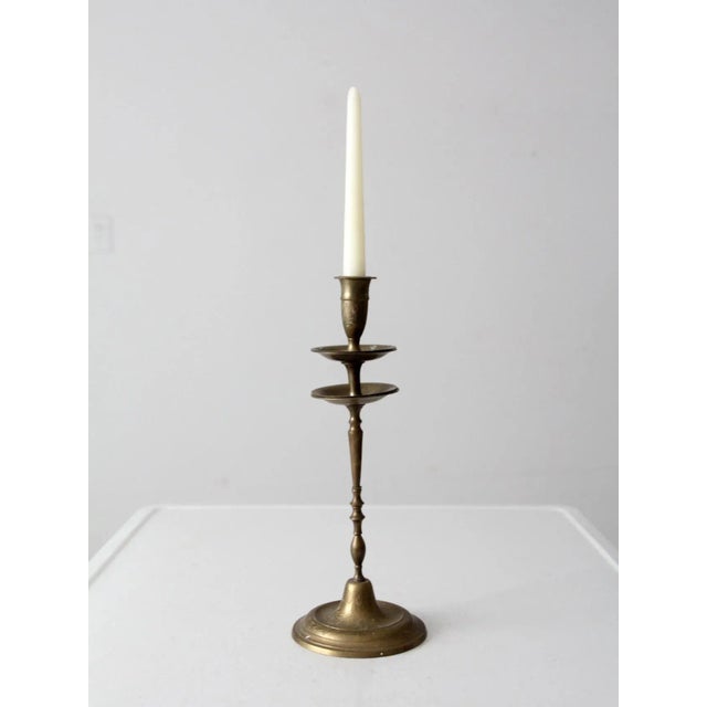 A vintage brass candlestick holder featuring a tall, tapered form, an intricately etched floral base, and double drip...
