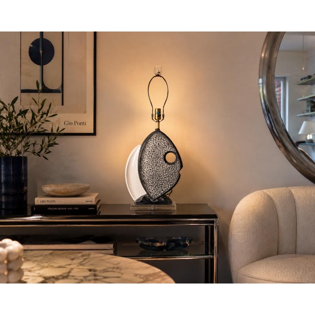 A striking 1980s Italian ceramic table lamp featuring an artistic pair of overlapping fish forms in contrasting textured...