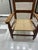 This is an antique or vintage handcrafted child's ladderback armchair with a woven rush or cane seat. Design: The chair...