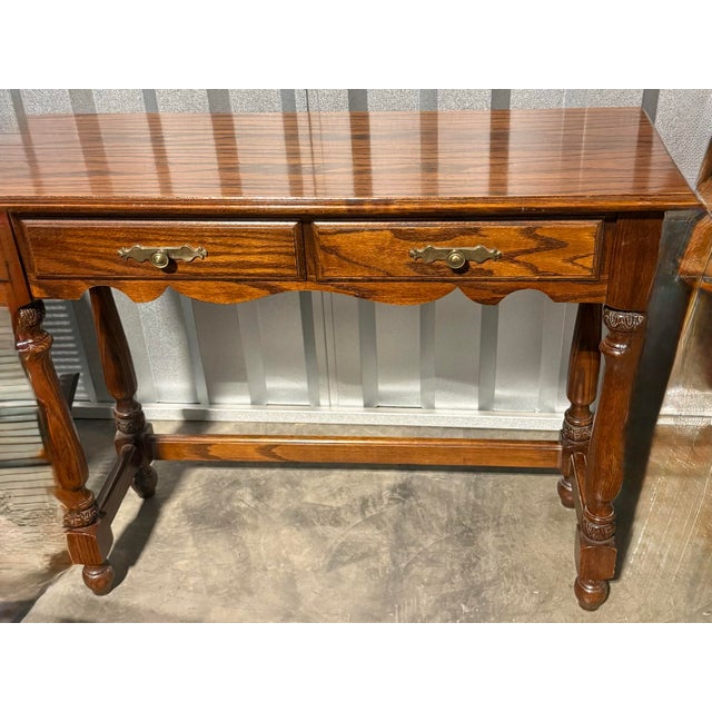 This elegant wooden console table features a rich oak grain finish, two utility drawers and distinctively carved turned...