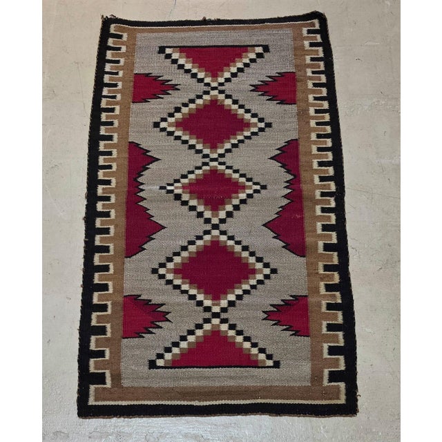 Southwestern-style handwoven wool rug featuring a striking geometric design in rich burgundy red, warm taupe gray, camel...