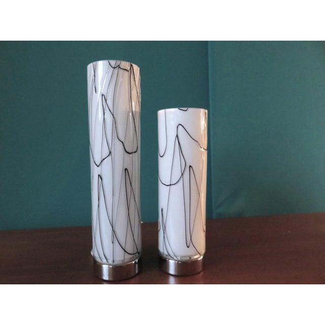 A twin-cylinder lamp, with two diffusers measuring 20 cm and 25 cm, made from white glass decorated with black glass paste...