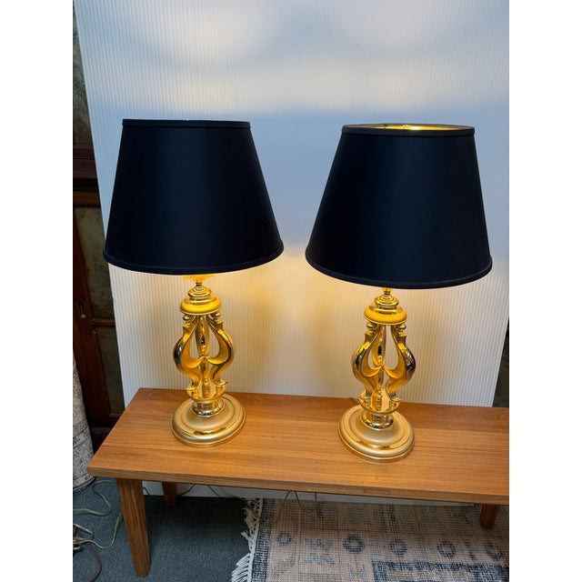 Design Plus Gallery presents a Pair of Sculpted Table Lamps with Regency Style. The lamps are dynamic with golden tall...