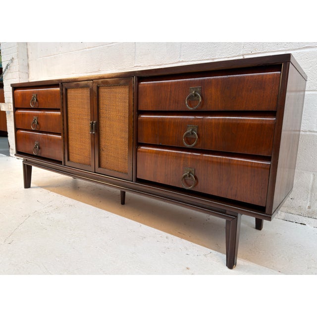 Elegant mid-century modern dresser featuring a rich walnut-toned finish, nine drawers, and a central two-door cabinet with...