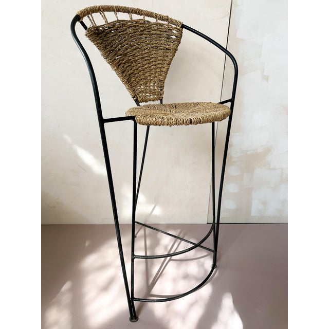 Contemporary stool featuring a metal structure combined with a woven rope seat. The design reflects a minimalist and...