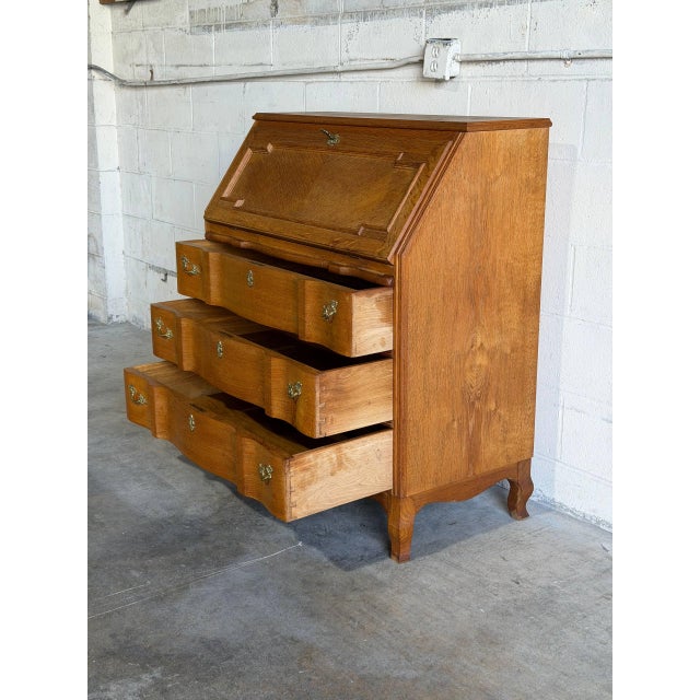 A slant drop-front writing surface opens to reveal internal small drawers and compartments over three deep lower drawers....