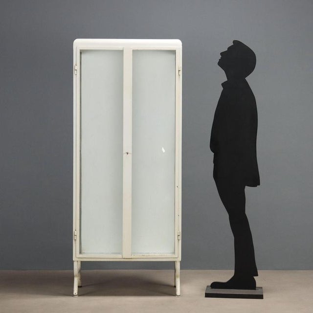 Enamelled iron display cabinet. Pair of glass front doors and sides, tubular legs. Missing internal shelves. Italy, first...