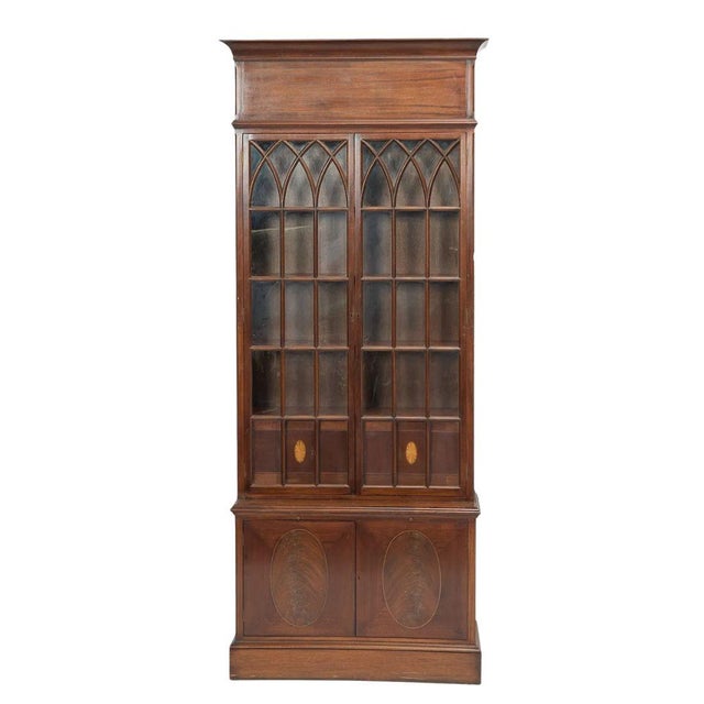 A tall English Gothic Revival bookcase, crafted in two parts and richly detailed throughout. The upper section is...