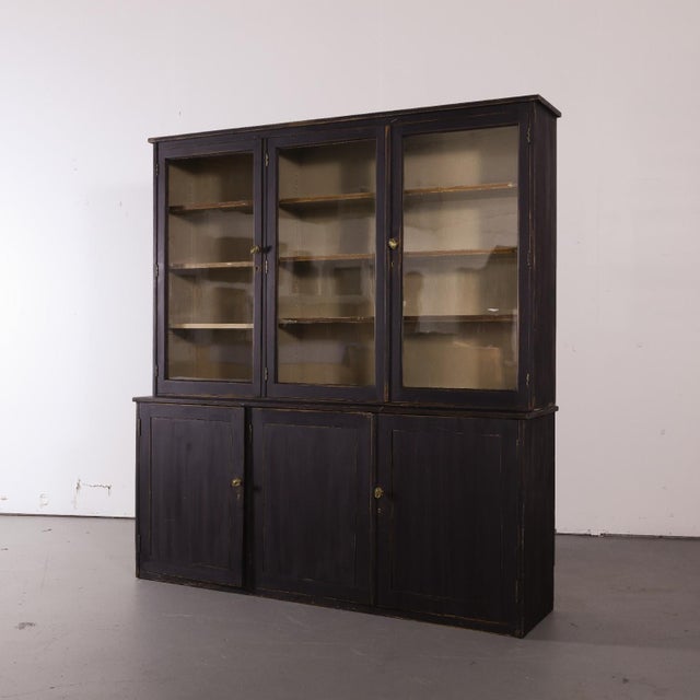 A substantial painted display cabinet with a painted black finish and warm wear showing through along the edges. The upper...