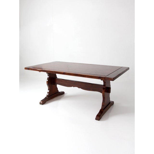 Vintage trestle dining table featuring a grounded, architectural base and a warm wood tone that lends a strong, inviting...