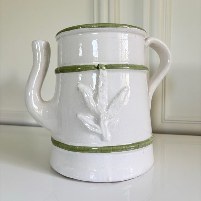 Stunning white glazed pottery pitcher featuring an elegant botanical relief design, accented with hand-painted green trim....