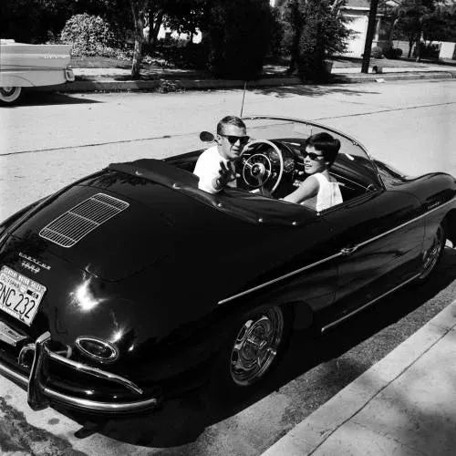 Steve McQueen and Neile Adams Smiling in Porsche This black and white capture features Steve McQueen waving hand while...