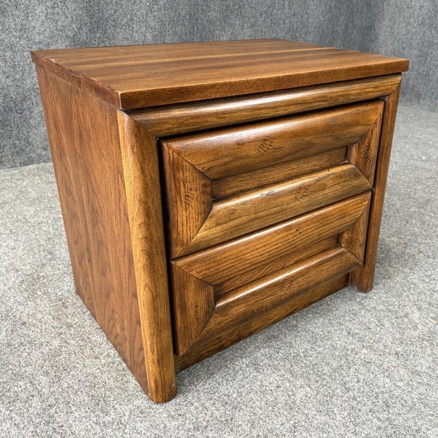 This Mid-Century oak nightstand features two drawers with bold sculpted fronts and a warm, natural wood finish. Its...