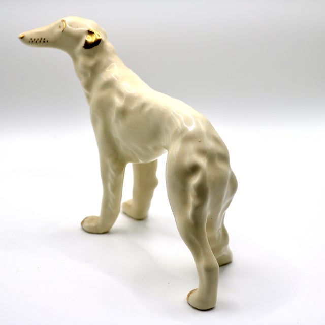 An elegant and sleek mid-century modern ceramic figurine depicting a standing greyhound or whippet. The sculpture features...
