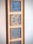 Tall framed art featuring individually inset batik patterned squares arranged in a vertical composition on a woven...