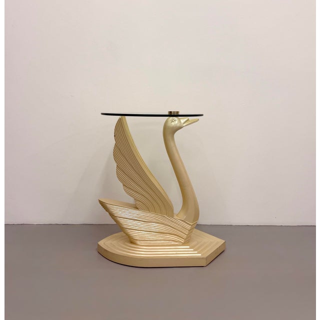 An elegant vintage accent table featuring a sculptural swan-form base with sweeping wings supporting a round glass top....
