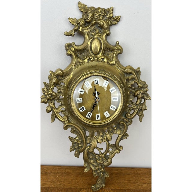 A beautifully decorative Vintage French brass hanging clock featuring an ornate floral and scrollwork design with elegant...