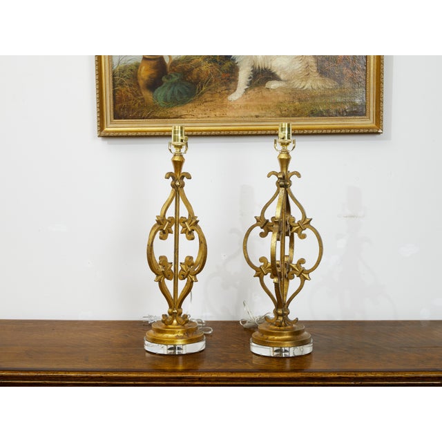 A pair of French gilt metal table lamps from the mid 20th century, with scrolling effects, fleurs de lys and lucite bases....