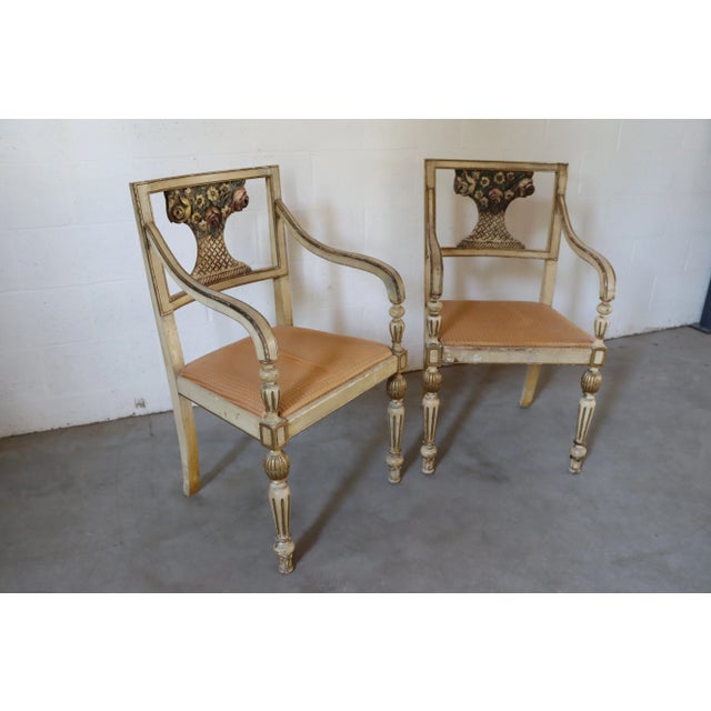 A pair of Italian arm chairs in cream with antique and gold gilded finish, flower basket design on back.