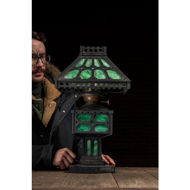 Arts and Crafts table lamp featuring a substantial cast iron framework fitted with vibrant green slag glass panels...