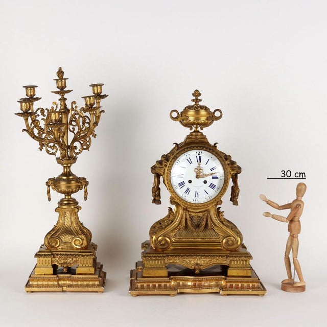 Triptych clock in gilded and chiseled bronze with carved and gilded wooden bases. The clock with a large rectangular base...