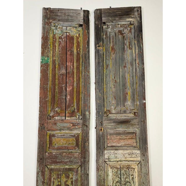 Pair of 19th century wooden doors with a heavily weathered and distressed appearance. They have intricate carved details,...