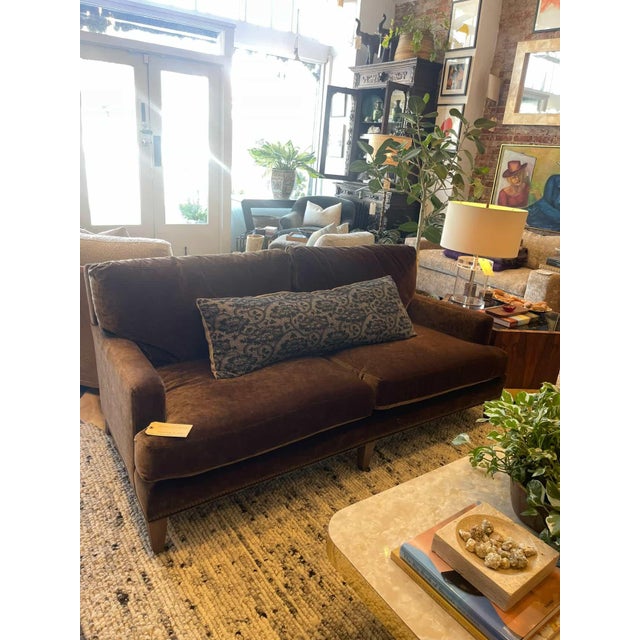 A rich brown velvet sofa with a deep, moody tone and plush, relaxed cushions. Clean arms and tapered wood legs set on...