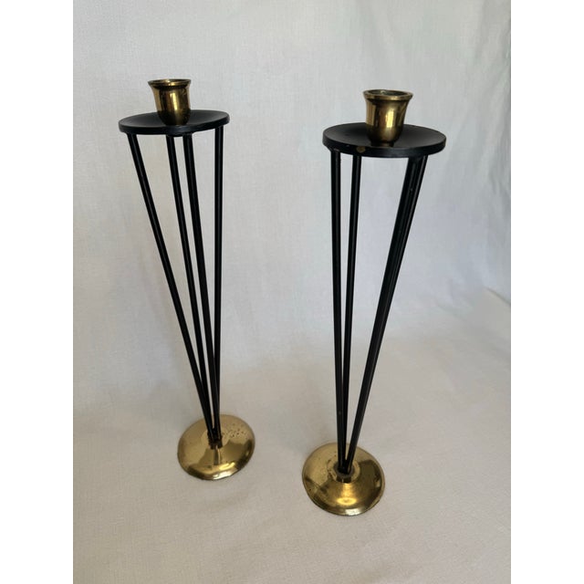 The pair of vintage tall mid century modern style candlesticks are comprised of painted black metal and polished brass in...