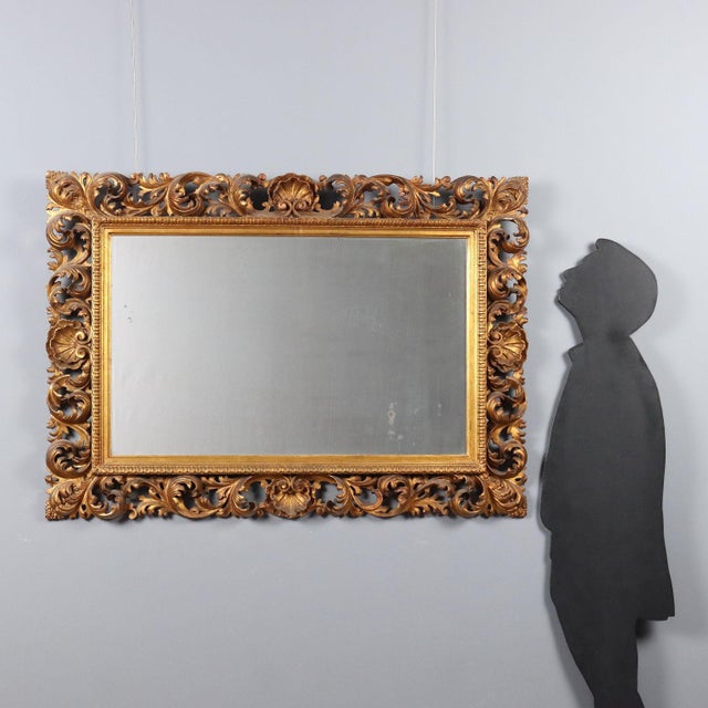 Baroque-style carved and gilded mirror, dating back to the early 20th century, made in Italy. The molded frame features an...
