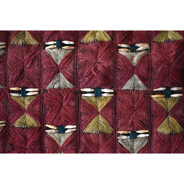 A vintage pillow cover, hand-embroidered with red, cream, and yellow threads in a geometric pattern, with natural seed...