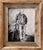 This artwork depicts a solitary figure in a cowboy hat, standing thoughtfully beside a stable, exuding a sense of quiet...